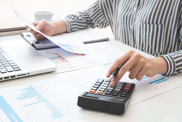 Business woman using calculator and writing make note with calculate. taxes and economic concepts. Savings, finances and economy concept through a laptop.