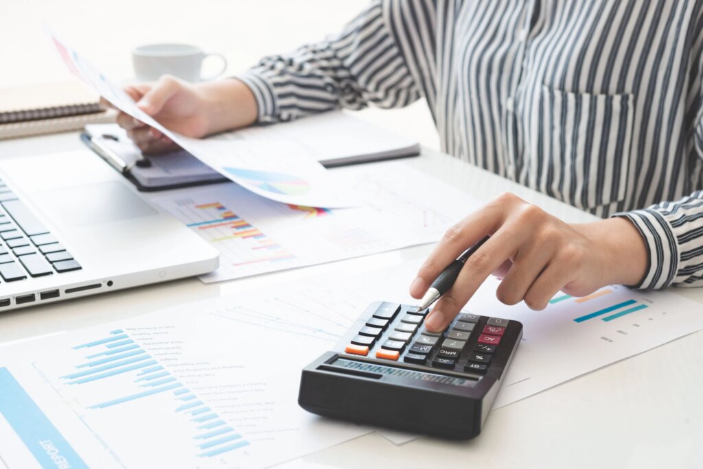 Business woman using calculator and writing make note with calculate. taxes and economic concepts. Savings, finances and economy concept through a laptop.