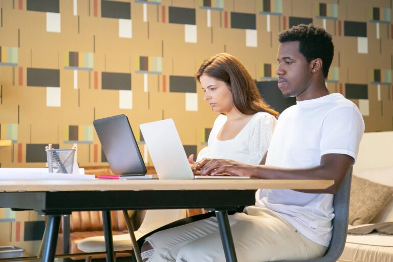 Un homme et une femme assis côte à côte à une table dans un espace de cowrking, ils sont concentrés et travaillent chacun sur leur ordinateur portable respectif