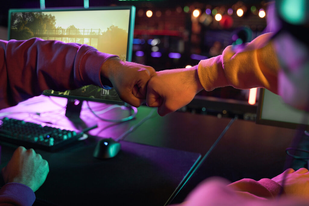 Formation e-sport - gros plan sur les mains de deux gamers qui célèbrent une victoire en faisant un "fist-bump", en arrière plan les écrans d'ordinateurs sur lesquels ils jouaient