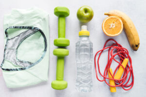 Sport santé - blog - vue du dessus d'objets de sport disposés de manière ordonnée : t-shirt plié, petites haltères vertes, gourde, pomme verte, banane, corde à santé et demi-orange