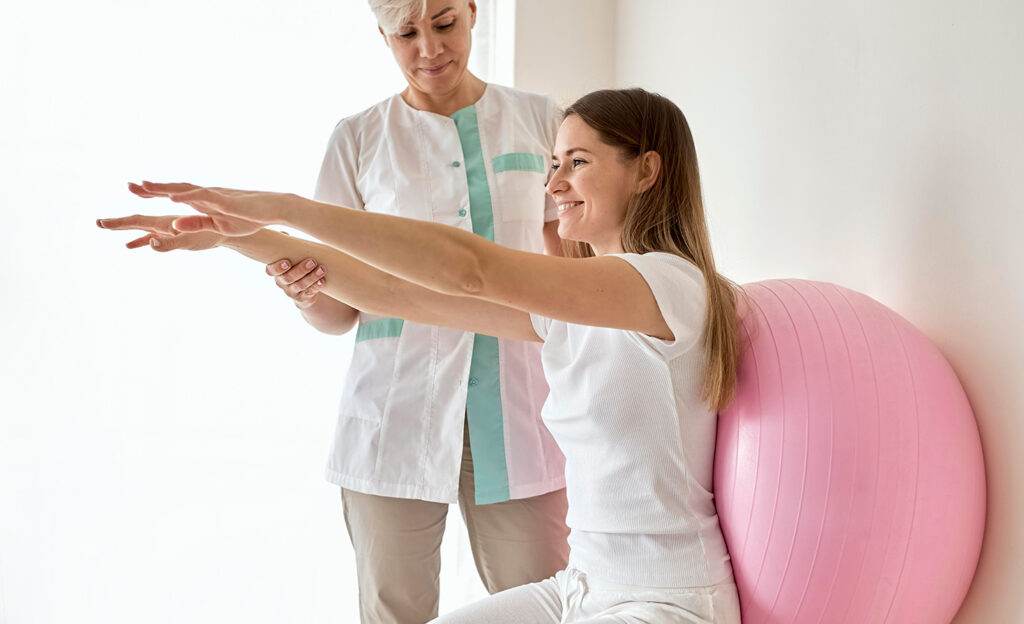 Sport sur ordonnance - blog - Une femme médecin accompagnant une autre femme lors d'une thérapie par le sport incluant l'utilisation d'un ballon de yoga rose