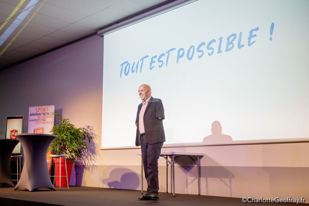 Philippe CROIZON sur scène devant un écran où est projetée la phrase "Tout est possible !" lors de la conférence sur le handicap organisée par FORMAPI Chalon