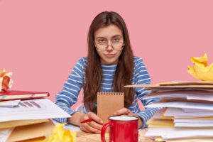 Rentrée 2024 - Blog - Jeune étudiante assise de face à un bureau sur lequel sont des piles de paperasse